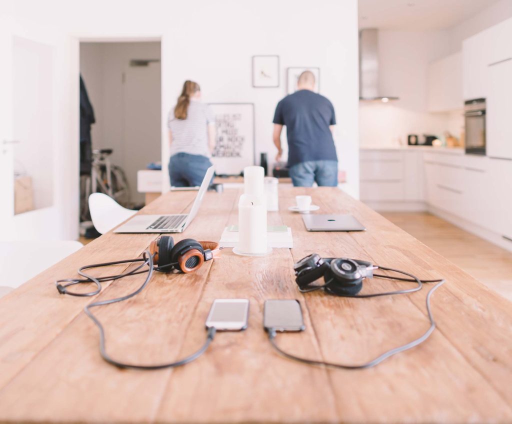 A table with headphones, smartphones, and cables in a modern kitchen setting.