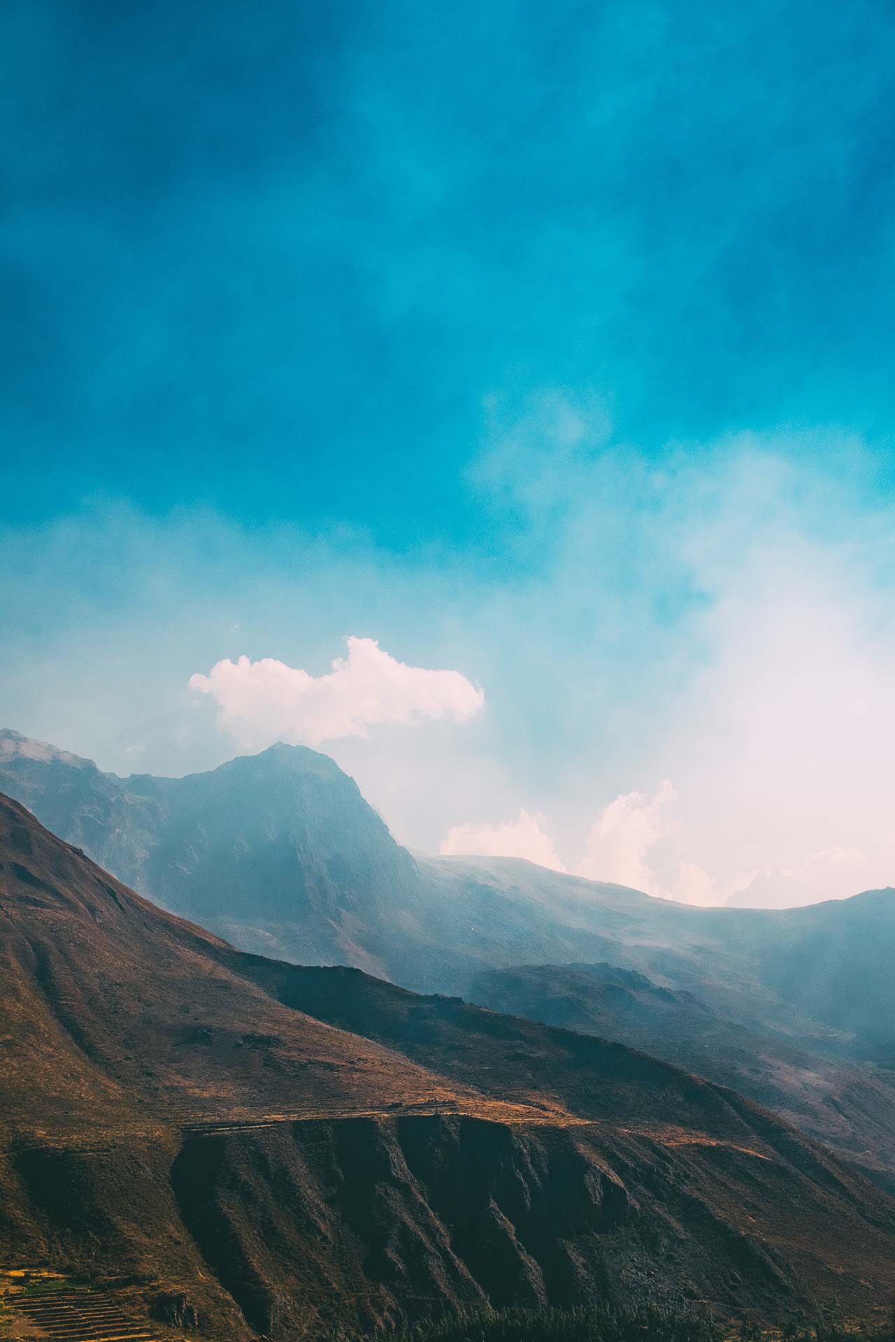A serene mountain landscape under a bright blue sky with scattered clouds.