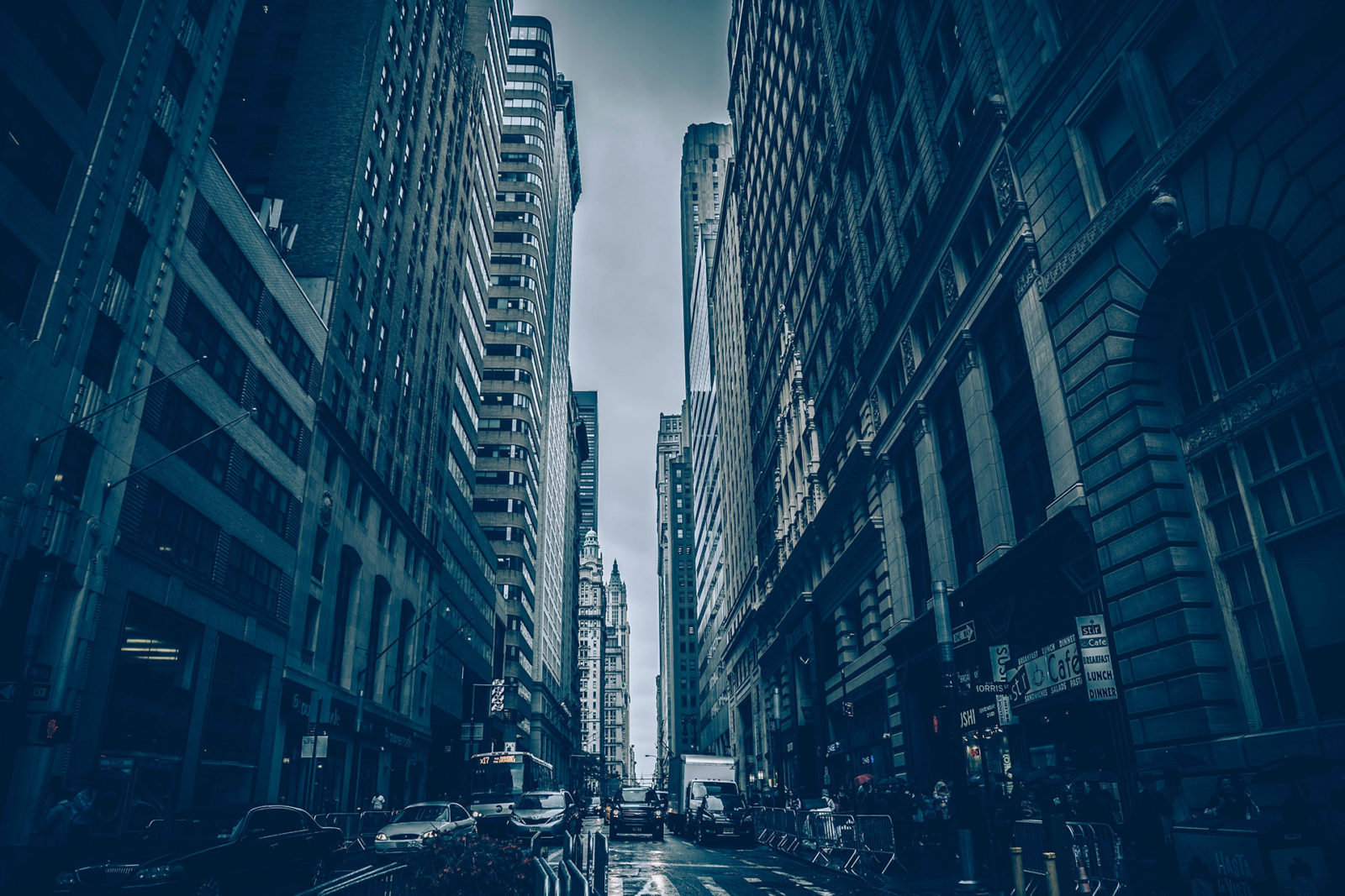 A busy city street flanked by tall buildings under a cloudy sky.
