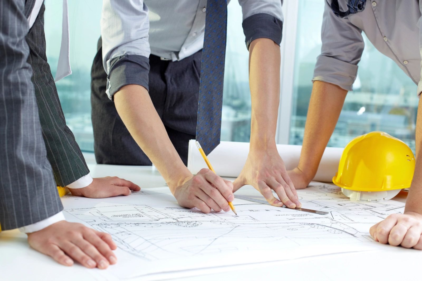 Hands working on architectural blueprints at a collaborative meeting.