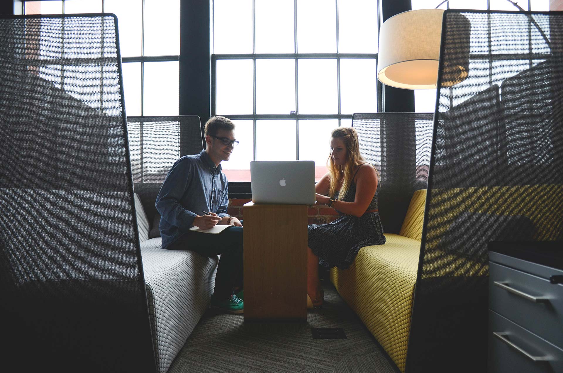 Two people having a discussion in a modern office space with a laptop.