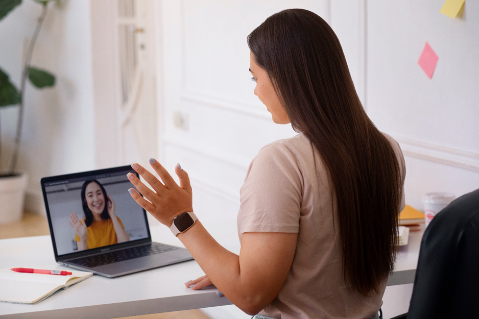 Woman video chatting on a laptop, waving hello.