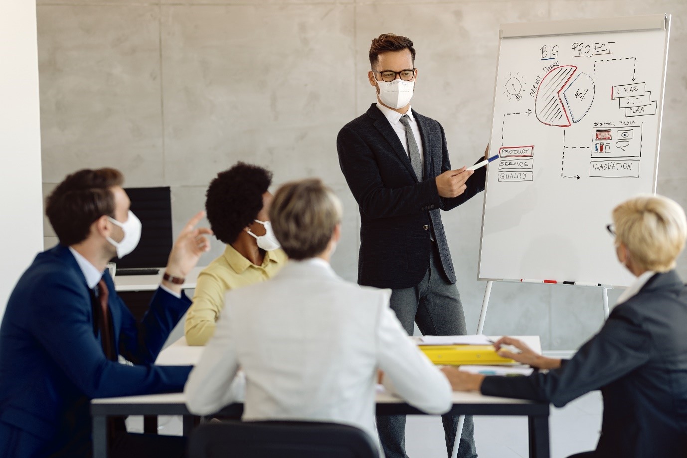 Businessman presenting to a small group in a meeting room, wearing a face mask.